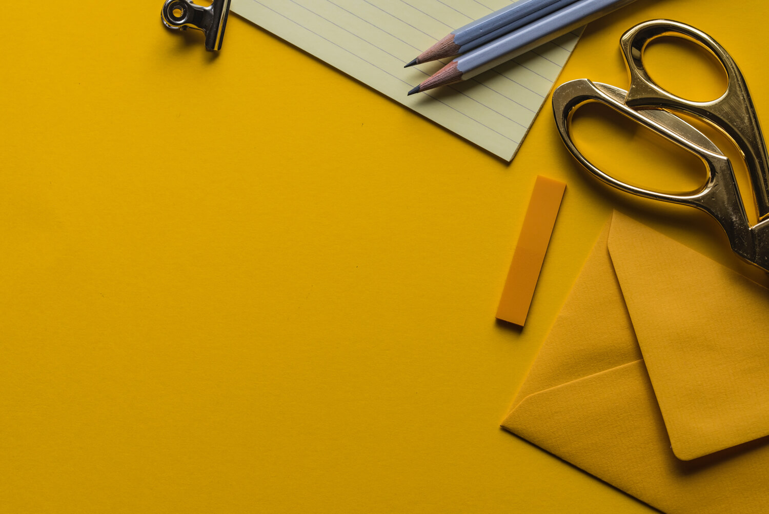 a photo of scissors, notebook and envelopes at the yellow background