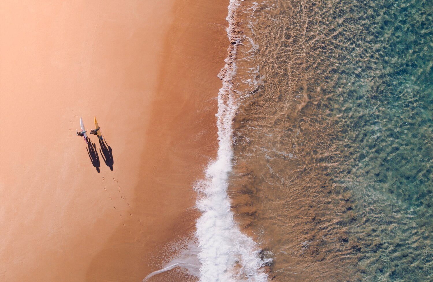 two surfers walking along the beach and the ocean to the right from them